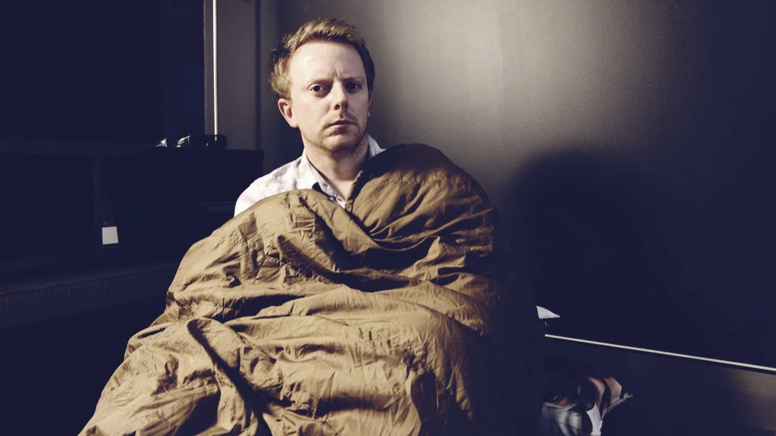 A man sitting up with a sleeping bag wrapped around him