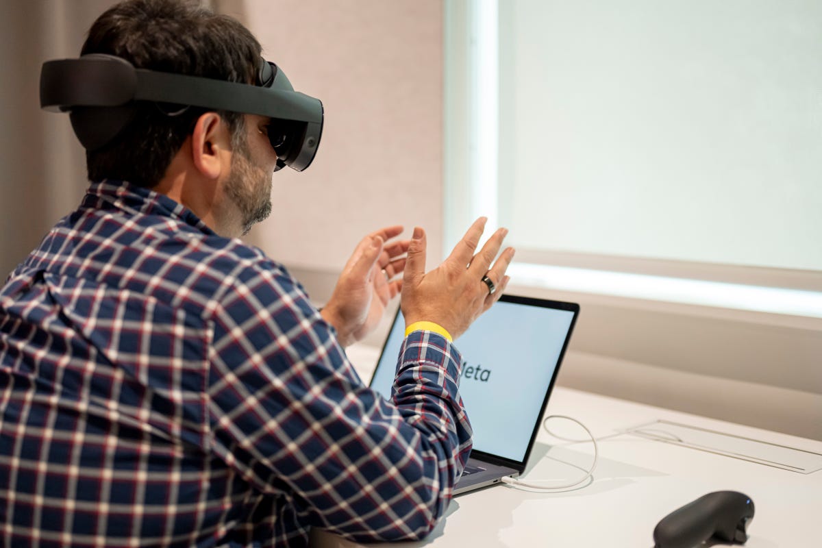 A man sitting at a desk wears the Quest Pro VR headset