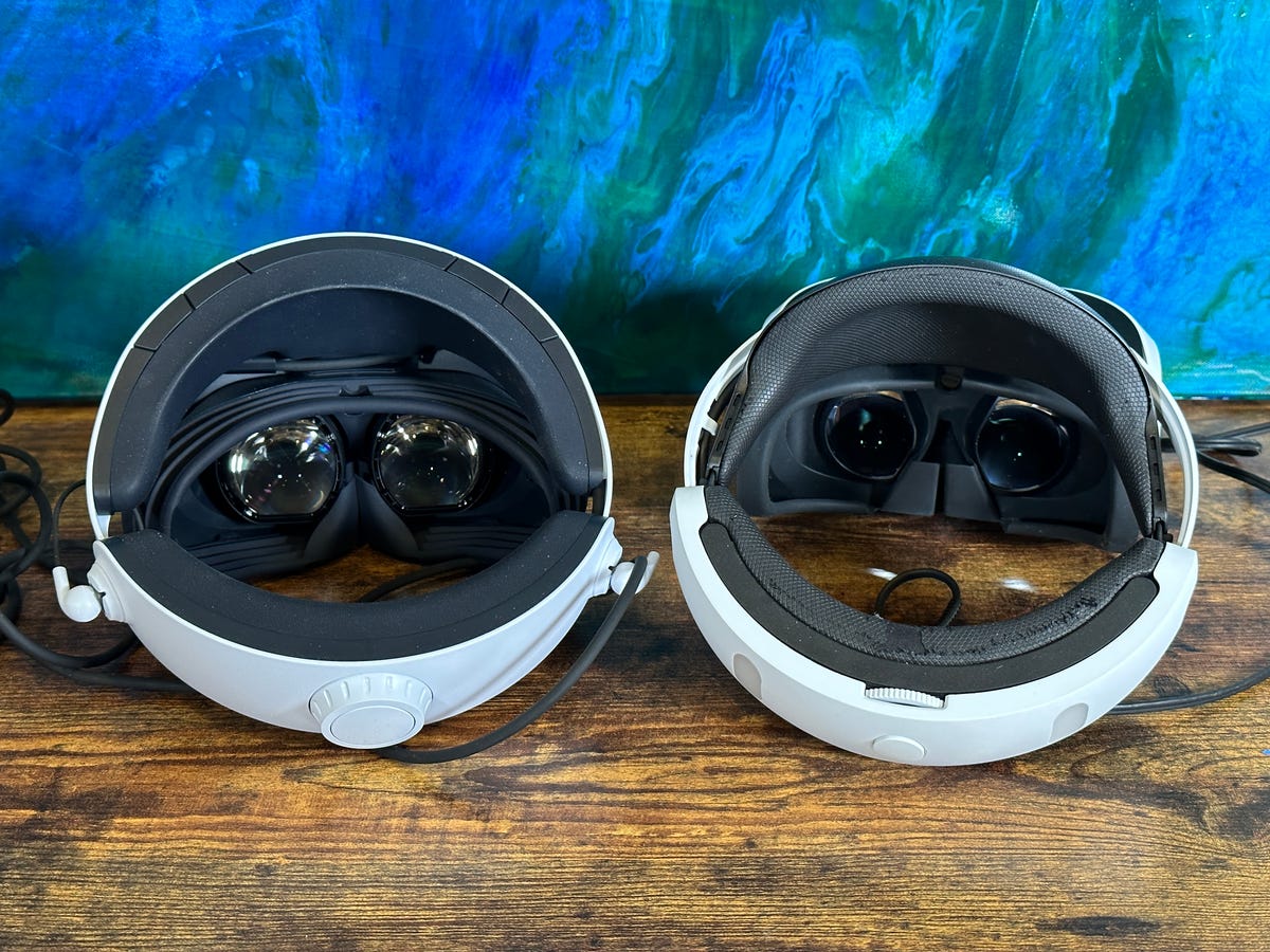 Two PlayStation VR headsets on a wood table, turned so we can see the lenses on each