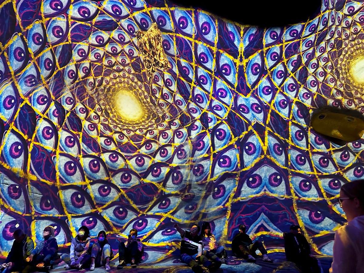 People sitting down in front of a giant projected art display on the wall behind them