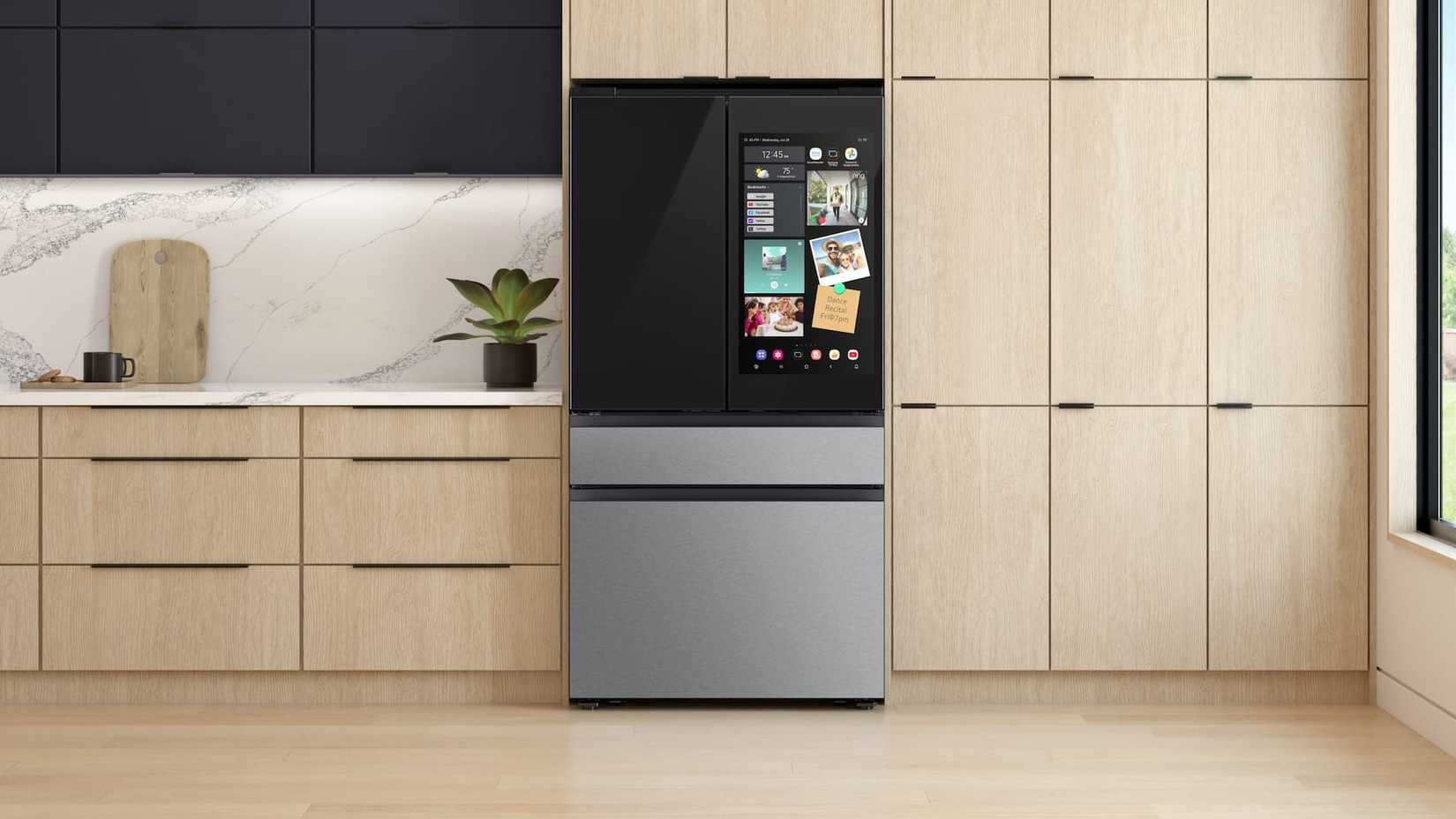 A Samsung fridge in the middle of a kitchen with its screen on